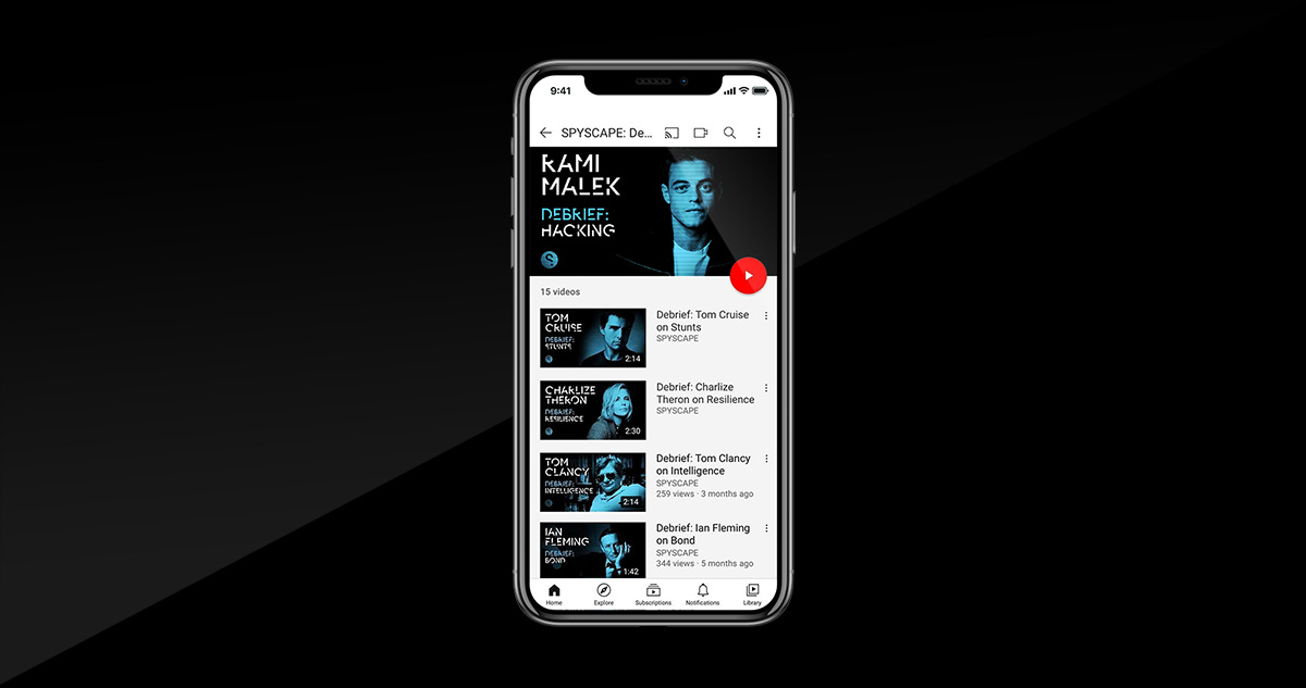 Smartphone displaying a YouTube playlist with video thumbnails and titles about debriefs featuring Tom Cruise, Charlize Theron, Tom Clancy, and Ian Fleming.